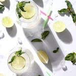 Overhead view of lemon-mint beverages with fresh lime slices and mint leaves on a white background.